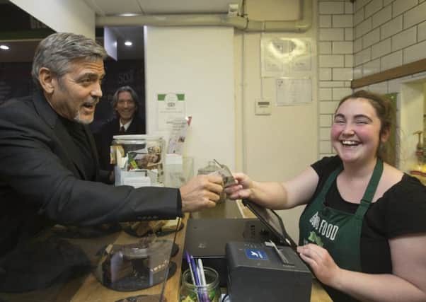 Hollywood star George Clooney hands over a five pound note to Ciara Whelan during a visit to Social Bite, a social enterprise cafe in Edinburgh. Picture: Getty