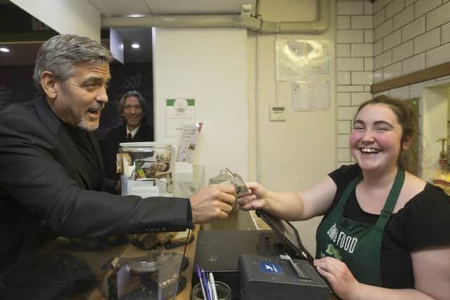 Hollywood star George Clooney hands over a five pound note to Ciara Whelan during a visit to Social Bite, a social enterprise cafe in Edinburgh. Picture: Getty