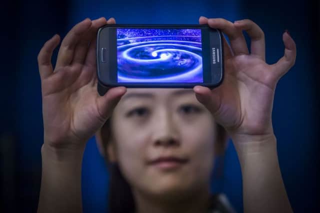 Student Muzi Li at the Institute of Gravitational Research at Glasgow University holding a phone that shows a computer simulation of gravity waves. Picture: PA