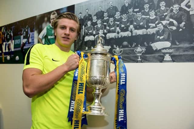 Jason Cummings poses with the trophy in front of the last Hibs side to win the Scottish Cup. Photograph: Paul Devlin/SNS