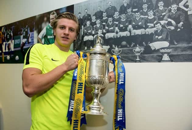 Jason Cummings poses with the trophy in front of the last Hibs side to win the Scottish Cup. Photograph: Paul Devlin/SNS