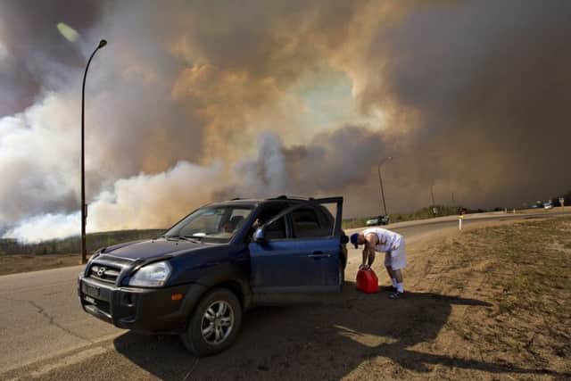 An evacuee puts petrol into his car on his way out of Fort McMurray, Alberta, as a wildfire burns in the background. Picture: Jason Franson/The Canadian Press via AP