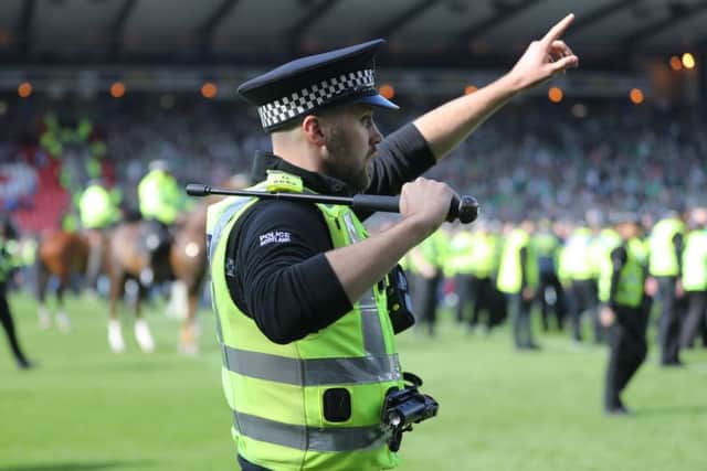 A policeman draws his baton as Hibs and Rangers fans invade the pitch at the final whistle after the Scottish Cup final. Picture: Getty