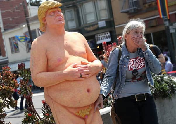 A passerby has a picture taken with a statue depicting Donald Trump in the nude in San Francisco. Picture: Getty Images