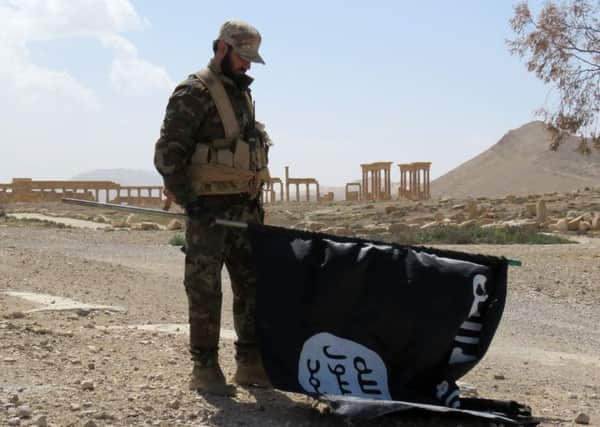 A member of the Syrian pro-government forces carries an Islamic State (IS) group flag as he stands on a street in the ancient city of Palmyra after troops recaptured the city from IS jihadists.
 Picture: Getty
