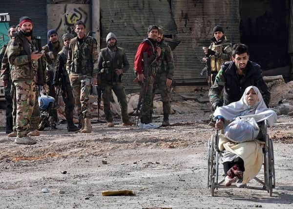 A member of the government forces pushes an injured woman in a wheelchair as civilians are evacuated from Aleppo's al-Shaar neighbourhood. Picture: Getty Images