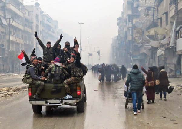 Syrian pro-regime fighters, gesture as they drive past resident fleeing violence in the restive Bustan al-Qasr neighbourhood, in Aleppo's Fardos neighbourhood after regime troops retook the area from rebel fighters. Picture: Getty Images