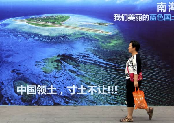 A woman walks past a billboard featuring an image of an island in the South China Sea. Picture: Chinatopix via AP, File