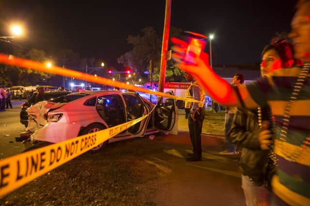 Parade goers walk by a wrecked car as New Orleans police work at the scene. (Chris Granger/AP)