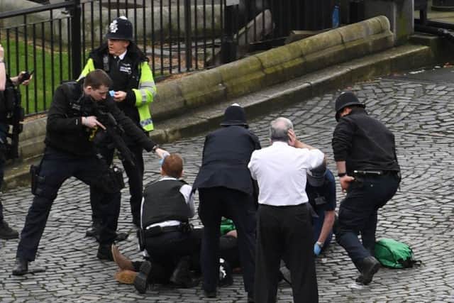 A policeman points a gun at a man on the floor at the top of the frame as emergency services attend the scene outside the Palace of Westminster. Picture: PA