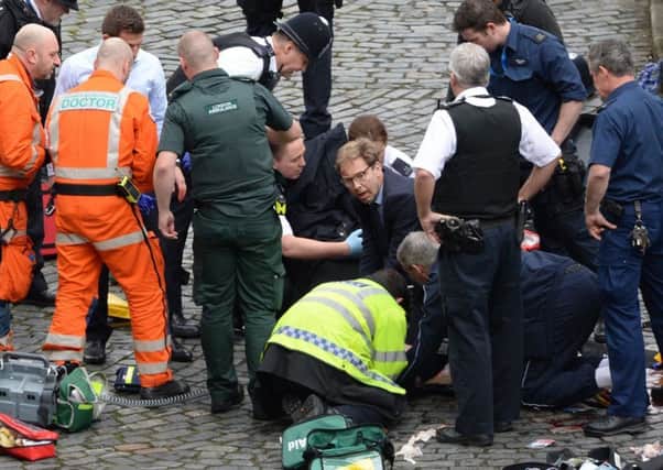Conservative MP Tobias Ellwood (centre) helps emergency services attend to a police officer outside the Palace of Westminster. Picture: PA