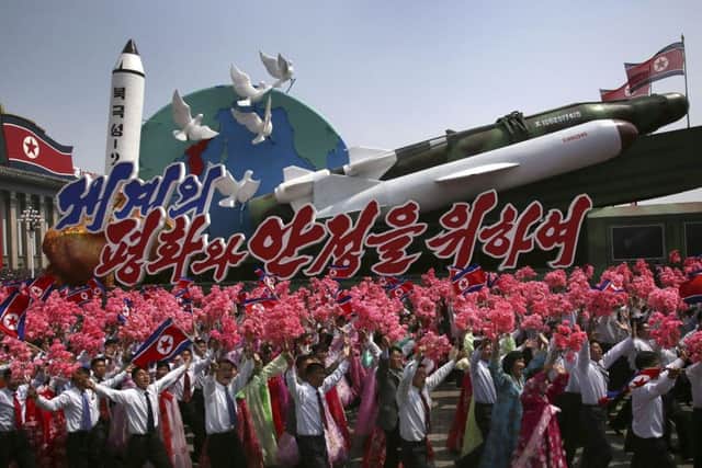 North Korean men and women wave flags and plastic flowers as a float with model missiles and rockets with words that read "For Peace and Stability in the World" is paraded. (AP Photo/Wong Maye-E)