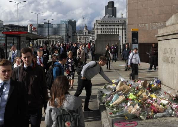 A man places flowers as commuters walk past flowers and messages for the victims of the London attacks as they cross London Bridge. Picture; Getty