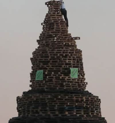 A man climbs a bonfire to plant an Irish tricolour on top of a bonfire pyre. Picture: PA Wire