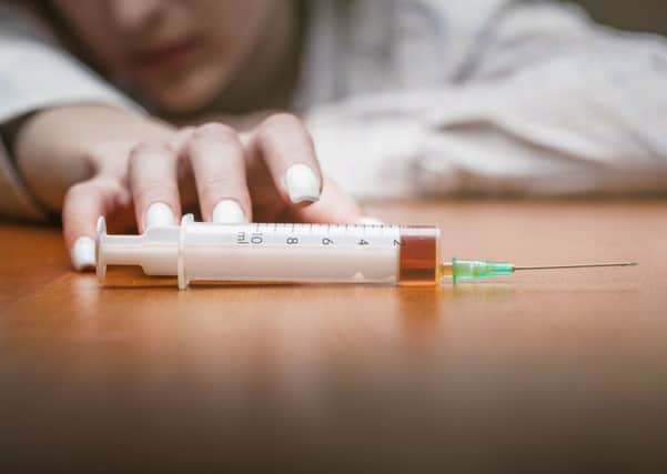 Close-up of a syringe with drugs beside lies a young woman. Focus on the syringe