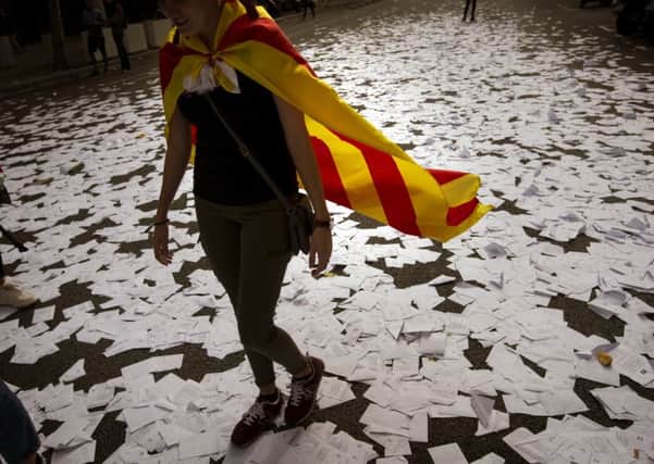 A supporter of Catalan independence walks along a street covered with referendum ballots thrown by demonstrators during a rally in front of the ruling Spanish Partido Popular party headquarters in Barcelona. Picture: Emilio Morenatti/AP