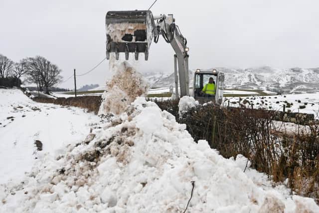 A man clears the B818 with a digger in Fintry as police advised motorists to drive with caution while weather warnings persist. Picture: Getty