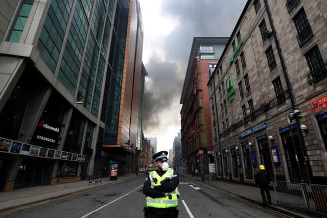 A police officer on Sauchiehall Street as firefighters work to control a blaze. Pic: PA Wire