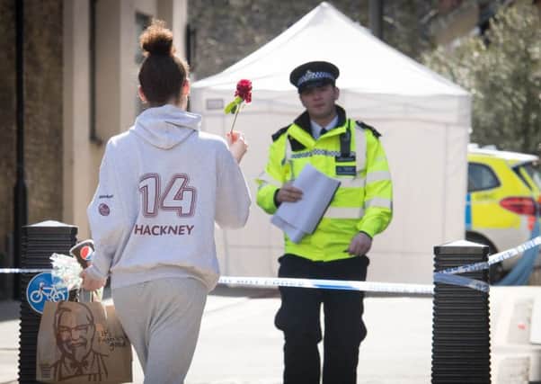 A woman brings a flower to the scene of a fatal stabbing in Hackney, east London