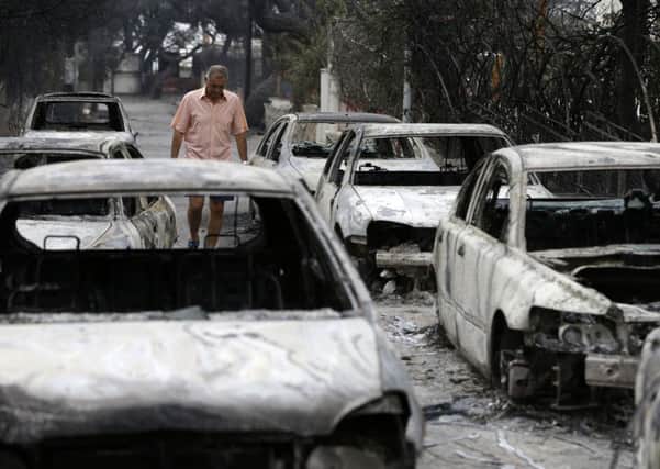 A man passes burned cars in Mati, east of Athens. Gale-fanned wildfires raged through holiday resorts near Greece's capital, killing at least 24 people by early Tuesday and injuring more than 100, including 11 in serious condition, in the country's deadliest fire season in more than a decade. Picture: AP Photo/Thanassis Stavrakis