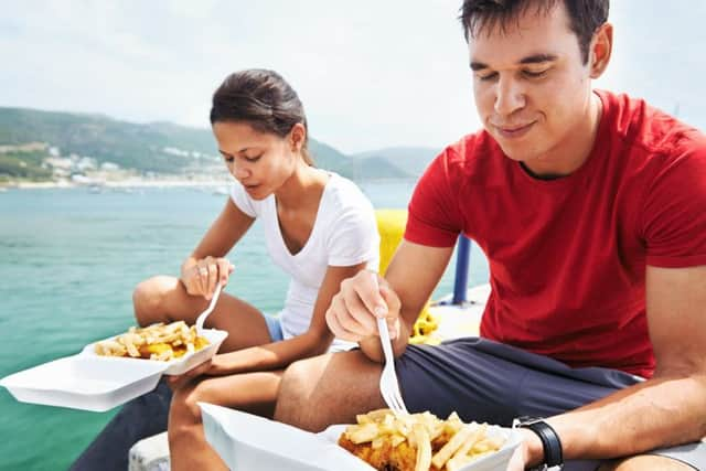 A couple sitting together by the harbour eating take away fish and chips.