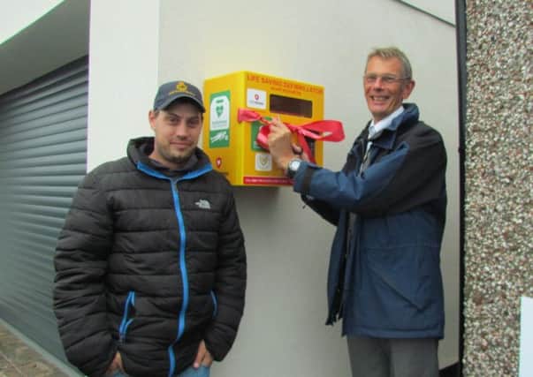 Andrew Binns and Ian Craighead cutting the ribbon at the unveiling of Burnmouth's second defibrillator on a wet evening at Lower Burnmouth.