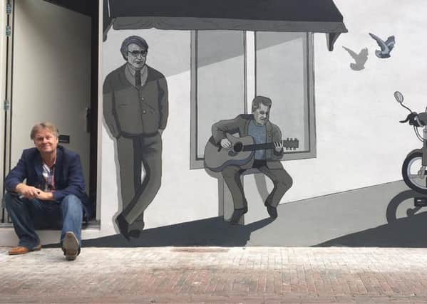 Artist Eric J Coolen next to his mural in Haarlem featuring Paul Murdoch playing guitar.