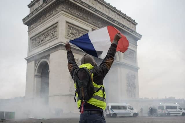 A protestor holds a french flag amid tear gas in front of the Arc de Triomphe near the Champs Elysees, in Paris. Photo by Lucas BARIOULET / AFP / LUCAS BARIOULET/AFP/Getty Images