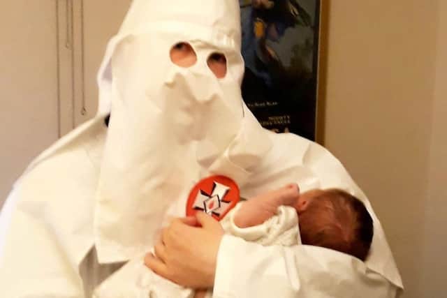 Adam Thomas holds a baby whilst wearing a Ku Klux Klan outfit. Picture: SWNS