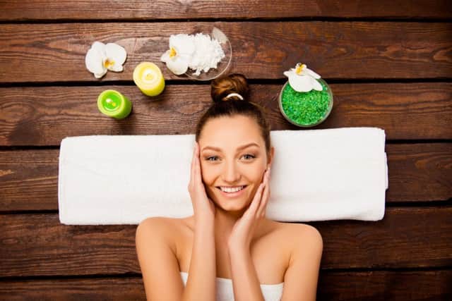 Top view of nice young woman laying in spa salon relaxing touching face