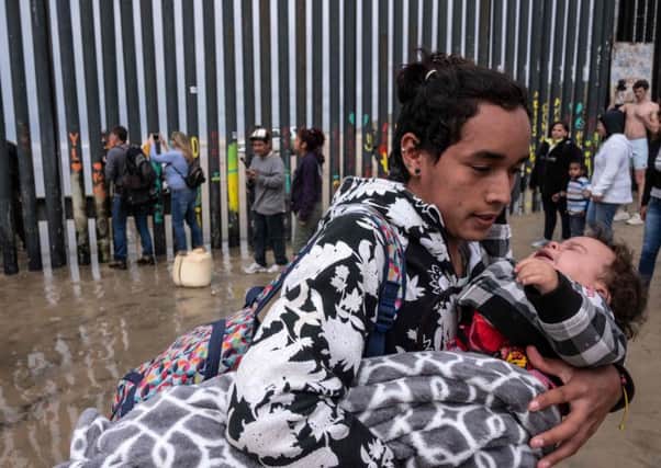 A Central American migrant carries a child after US Border Patrol sprayed them with pepper spray as they tried to cross the US-Mexico border fence (Picture: Guillermo Arisa/AFP/Getty)