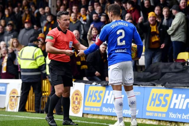 Rangers defender James Tavernier hands a lighter to referee Nick Walsh after it was thrown from the crowd. Picture: SNS
