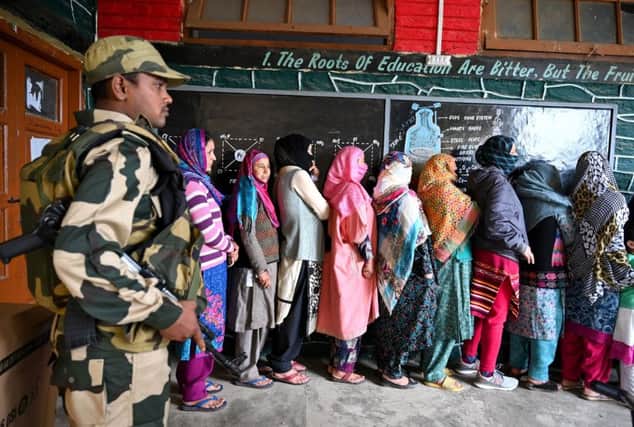 Kashmiri Muslim voters stand in a queue an as Indian Border Security (BSF) soldier walks past at a polling station during the first phase of India's general election in Handwara (Photo by Tauseef MUSTAFA / AFP)