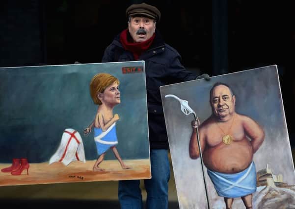 Artist Kaya Mar holds up his paintings of the two faces of the SNP, Nicola Sturgeon and Alex Salmond. Picture: Jeff J Mitchell/Getty
