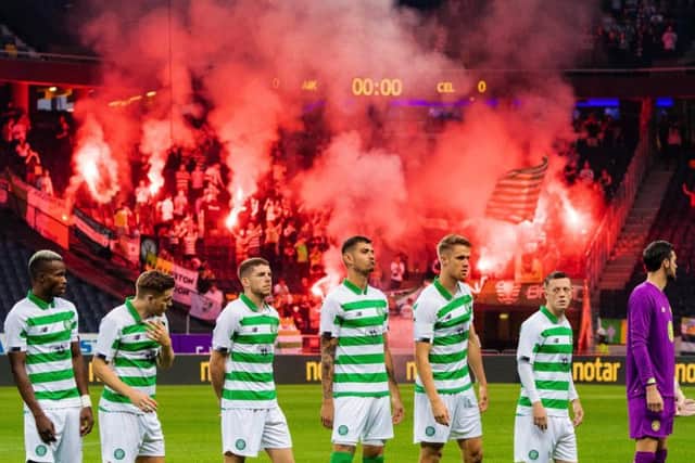 Celtic players line up for kick-off as supporters hold flares in the background. Picture: SNS