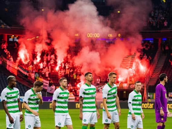 Celtic players line up for kick-off as supporters hold flares in the background. Picture: SNS