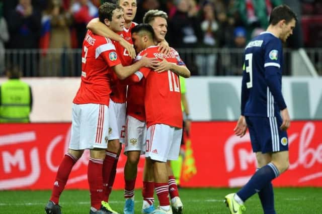 Aleksandr Golovin celebrates with teammates after scoring the fourth Russian goal as a dejected Andrew Robertson walks past.