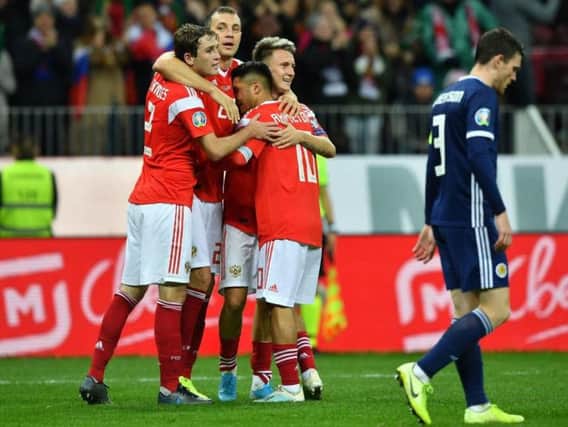 Aleksandr Golovin celebrates with teammates after scoring the fourth Russian goal as a dejected Andrew Robertson walks past.