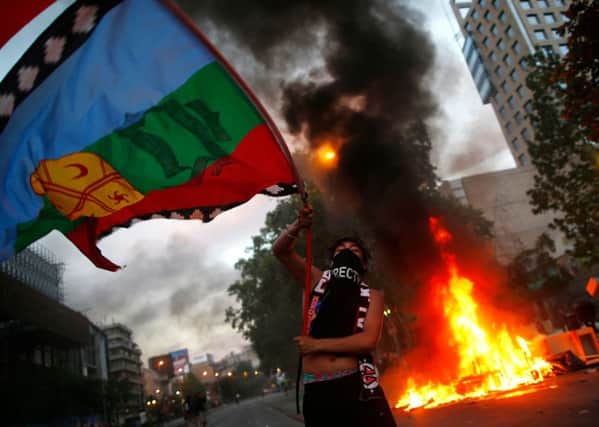 A demonstrator waves a Mapuche indigenous flag near a bonfire in Chile's capital Santiago amid protests over living costs and social inequality (Picture: Pablo Vera/AFP via Getty Images)