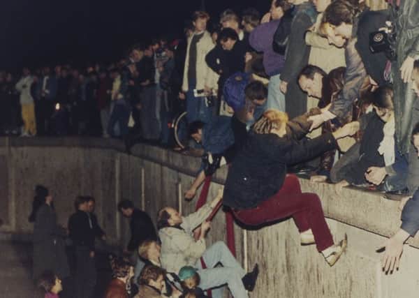 East Berliners get a helping hand from West Berliners as they climb the Berlin Wall. PIcture: Jockel Finck/AP