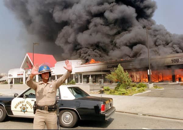 A California Highway patrolman directs raffic around a shopping mall engulfed in flames in April 1992, during the LA Riots. PIC: Carlow Chiebeck/AFP via Getty Images