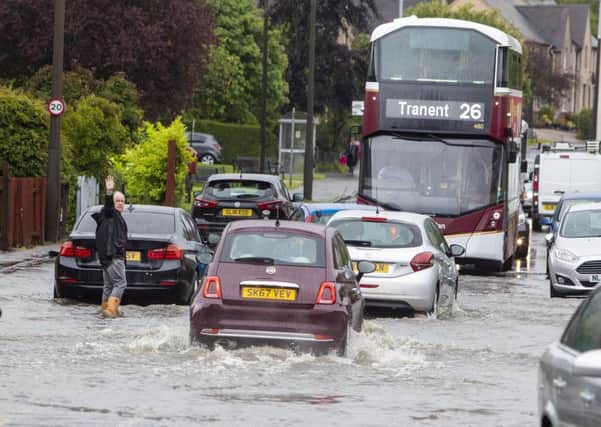 A man directs traffic through a flooded road in Barnton, Edinburgh, as heavy rains hit the country last June. Picture: SWNS